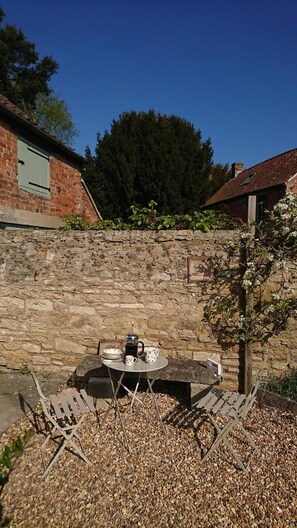A rustic outdoor seating area with a stone wall backdrop, a metal table with a coffee pot, and a bench. - Nr Devizes, Marlborough & Bath, , walled garden (Seend)