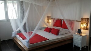 A bed with a canopy, red pillows, and a bedside table with a lamp. - Gite corossol Martinique private pool, naturist residence (Sainte-Luce)