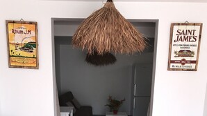 A living room with two white chairs, a hanging thatched ceiling light, and two wall-mounted signs advertising rum and Saint James. - Gite corossol Martinique private pool, naturist residence (Sainte-Luce)