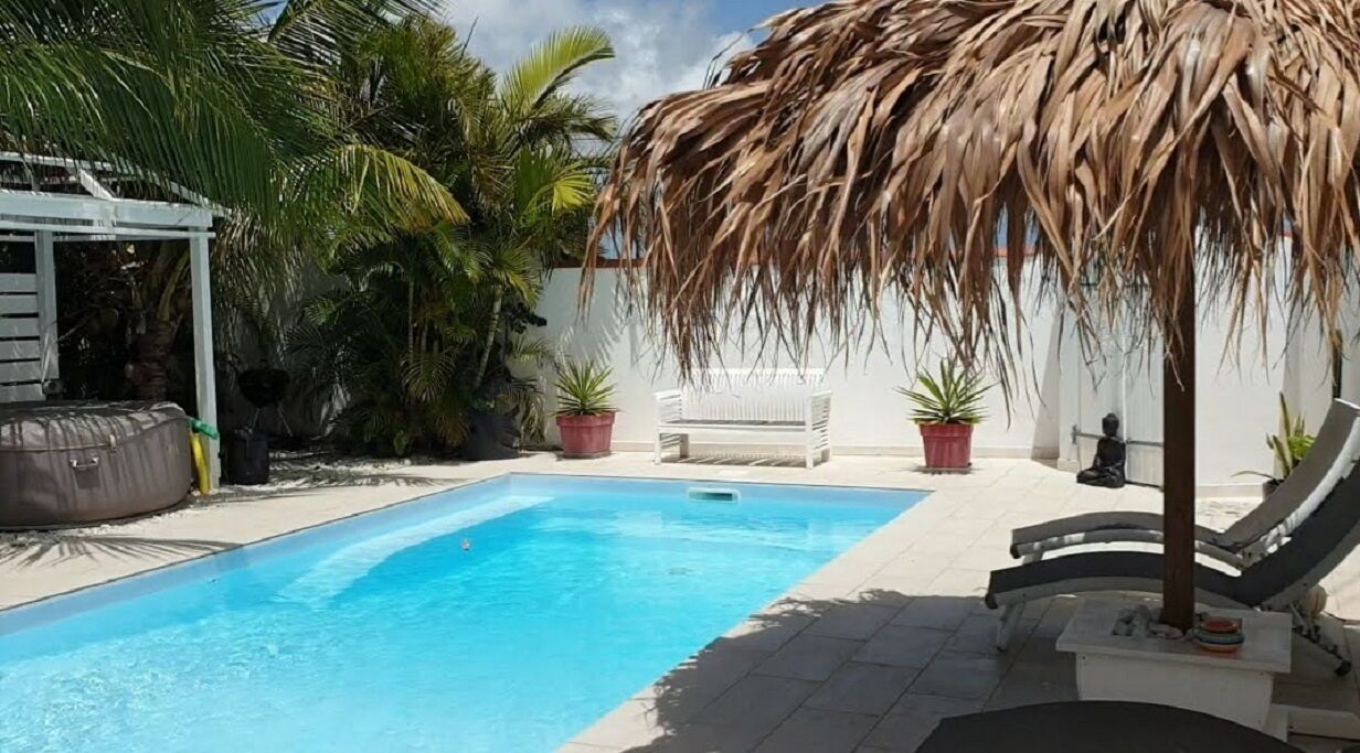A swimming pool with a thatched roof, surrounded by palm trees and potted plants.