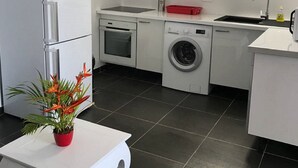 A modern kitchen with white cabinets, a built-in oven, a washing machine, and a sink. - Gite corossol Martinique private pool, naturist residence (Sainte-Luce)