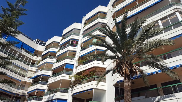 A multi-story building with balconies, some with plants.