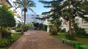 A paved walkway with benches, surrounded by greenery and buildings.