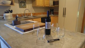 A kitchen counter with a wine bottle, glasses, a corkscrew, and a cutting board.