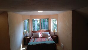 A bedroom with a bed, two nightstands, a lamp on each, and three windows providing natural light.