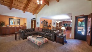 A spacious living room with a large sectional sofa, a patterned ottoman, and a wooden ceiling.