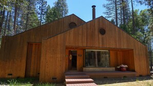 A wooden cabin with a large glass door, a chimney, and a small porch with steps leading to the entrance.