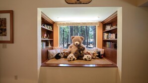 A cozy reading nook with a large teddy bear centerpiece, surrounded by bookshelves and a window with a forest view. - Bruin's Den (Wawona)
