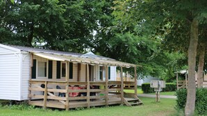 Een klein, gelijkvloers houten huisje met een veranda, omringd door bomen.