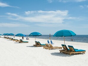 Una playa con filas de sillas de madera y sombrillas azules.