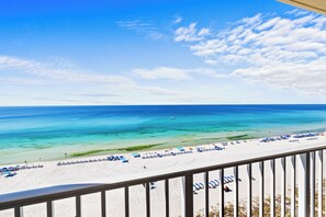 Une vue sur la plage depuis un balcon doté d’une balustrade, avec un ciel bleu clair et une mer turquoise.
