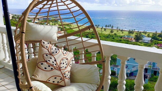 A wicker swing chair with cushions on a balcony overlooking a coastal view. - A Touch Of Class To Your Stay-Our Iconic Egg Chair. (Basseterre)