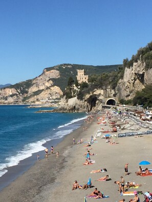 A beach with people sunbathing and swimming, a castle on a hill, and a tunnel entrance. - Sunny, updated apartment with balcony in Finalborgo and near gorgeous beaches  (Finalborgo, Finale Ligure)