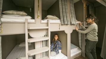 A bunk bed room with a person adjusting the curtains.