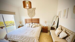 Et soveværelse med en stor seng, et træhovedgærde, et natbord med en vase, en rund måtte og en sofa med puder.