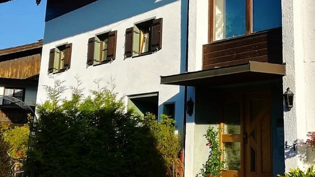 Un edificio a due piani con facciata bianca, persiane di legno e un balcone.