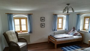 Una camera da letto con un letto in legno, una sedia in vimini, un termosifone e due finestre con tende.