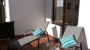 Una veranda con due poltrone, un tavolo, una finestra con tende e un pavimento piastrellato.