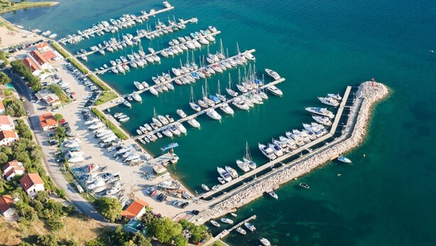 Vue aérienne d’une marina où sont amarrés de nombreux bateaux, avec un quai et des bâtiments adjacents.