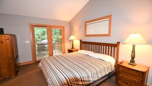 Un dormitorio con una cama, dos mesitas de noche con lámparas, un aparador de madera y una puerta corrediza de vidrio que da a un balcón.