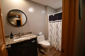 A bathroom with a sink, mirror, toilet, and shower curtain.