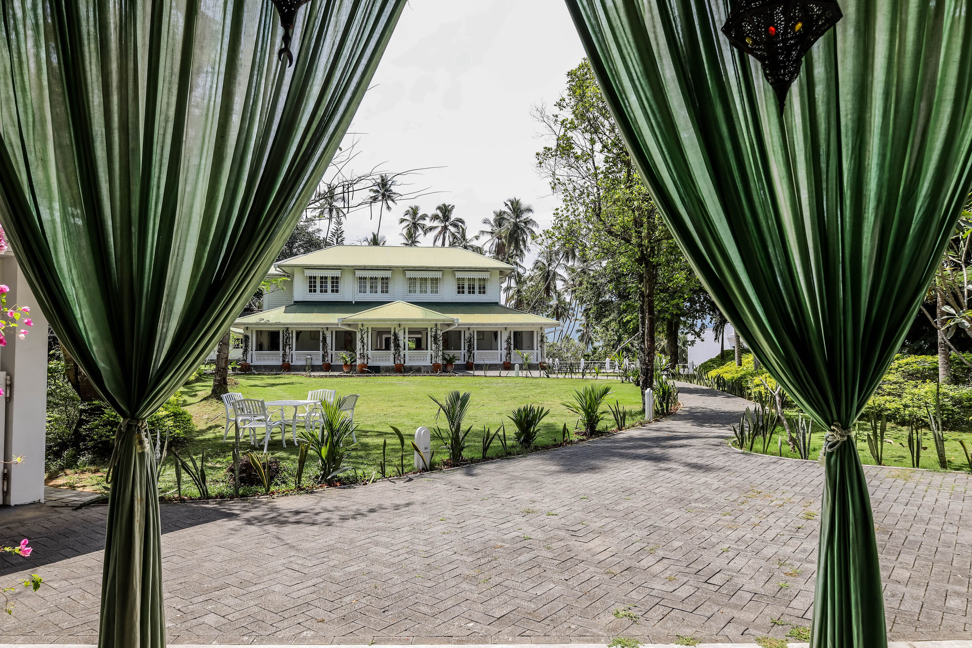 A large, two-story building with a green lawn and white exterior, surrounded by tropical vegetation.