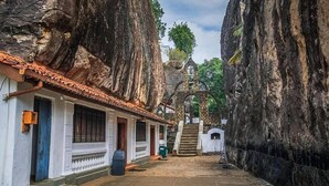 A narrow street flanked by tall rock walls with a building featuring a tiled roof and a staircase leading to a higher level. - The Flame Tree Estate & Hotel (Galagedara)