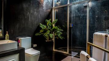 A modern bathroom with a black wall, a white sink, a toilet, a potted plant, a glass shower enclosure, and a towel rack.