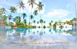 Vista despejada de una piscina con reflejos de palmeras y un cielo claro.