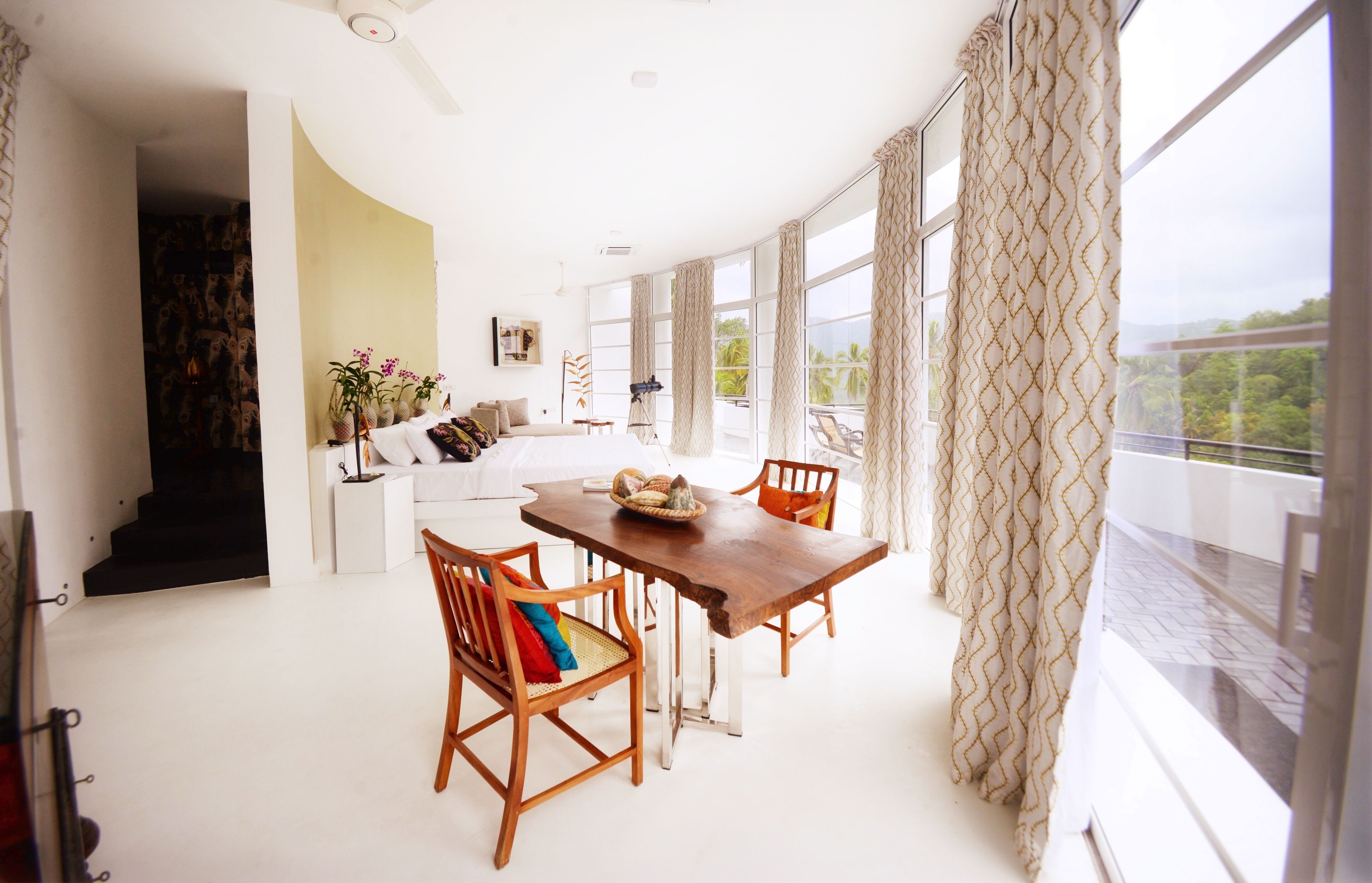 Um quarto espaçoso com uma grande mesa de jantar, duas cadeiras de madeira, um sofá e vista para o exterior através de amplas janelas.
