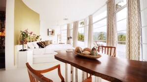 A modern living room with a curved white sofa, a wooden dining table with chairs, and a large window with curtains. - The Flame Tree Estate & Hotel (Galagedara)