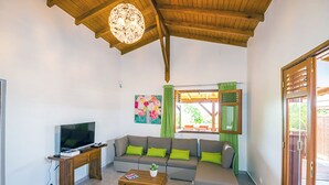 Un soggiorno con soffitto in legno, una televisione su un mobile in legno, un divano grigio con cuscini verdi, un tavolino da caffè in legno e un quadro appeso al muro.