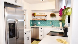 Une cuisine moderne avec un réfrigérateur en acier inoxydable, des meubles blancs, un pare-feu turquoise et un petit îlot agrémenté d’un objet décoratif doré.