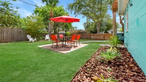 Un jardin avec une terrasse, un parasol rouge et du mobilier d’extérieur.