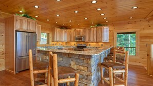 Interior de una cabaña de madera con cocina, que incluye una isla de piedra, taburetes de bar y electrodomésticos empotrados.