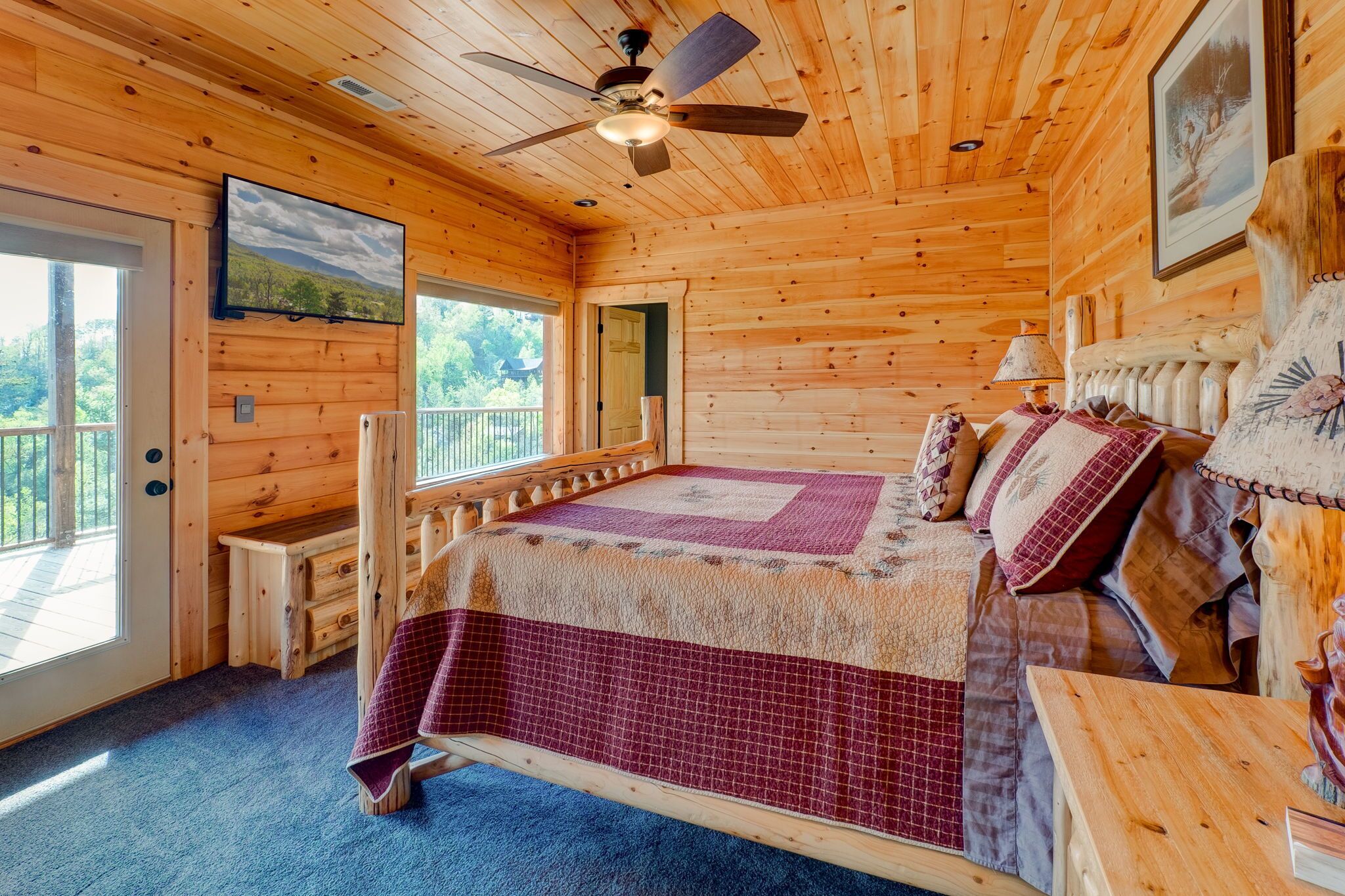 Un dormitorio de cabaña de madera con cama, ventilador de techo, ventana grande y puerta.