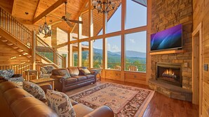 Amplia sala de estar con un sofá de cuero, chimenea y grandes ventanales con vistas a la montaña.