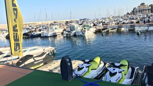 A marina with multiple boats docked, a jet ski in the foreground, and a yellow flag with text. - Apartment for 4 people terrace sea view Cambrils beach 230m (Cambrils)