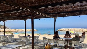An outdoor seating area with tables and chairs, overlooking a beach with a rocky shoreline and clear blue water. - Apartment for 4 people terrace sea view Cambrils beach 230m (Cambrils)