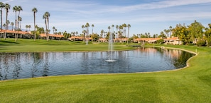 Ein Golfplatz mit Teich, Palmen und Hotelgebäuden.
