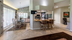 A spacious kitchen with a stone accent wall, a dining area with a chandelier, and a bar area with stools. - 
FUN IN SUN, GOLF&TEN.FEB-MARCH, PALM DESERT, PALM VALLEY CC. 55-Day Minimum
   (Palm Desert)