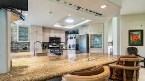 A spacious kitchen with granite countertops, stainless steel appliances, and wooden bar stools. - 
FUN IN SUN, GOLF&TEN.FEB-MARCH, PALM DESERT, PALM VALLEY CC. 55-Day Minimum
   (Palm Desert)