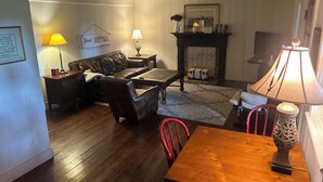 A cozy living room with a leather sofa, a wooden coffee table, and a fireplace. There is a lamp on the table and a framed picture on the wall. - Historical Farm Cottage Retreat near Clemson (Westminster)