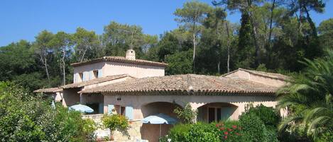 A Mediterranean-style villa with a tiled roof, stone walls, and a stone pathway leading to the entrance.
