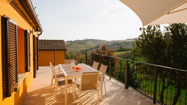 Una terrazza con tavolo e sedie, un ombrellone bianco e vista su dolci colline.