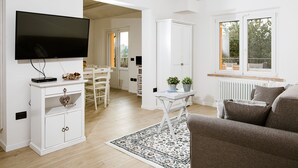 Un soggiorno moderno con una TV a schermo piatto, mobili bianchi, un tappeto decorato e vista sull'esterno attraverso una finestra.