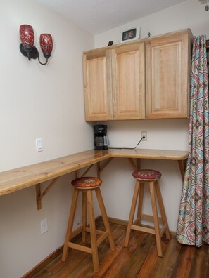 A small kitchen with wooden cabinets, a coffee maker, and two stools.