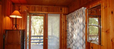 A wooden cabin interior with a wooden door, a lamp, a patterned curtain, and a window.