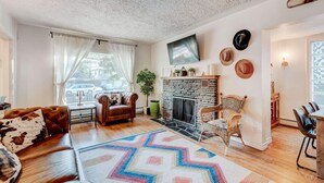 Un salon chaleureux avec une cheminée, un canapé en cuir et un coin repas comprenant une table et des chaises.