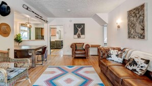 Un vaste espace de vie doté d’un plancher en bois, d’un canapé en cuir marron, d’un tapis à motifs et d’un coin repas avec une table et des chaises en bois.